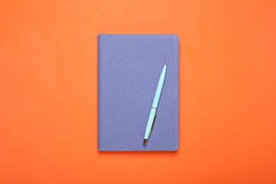 Photo of Closed blue notebook and pen on orange background, top view