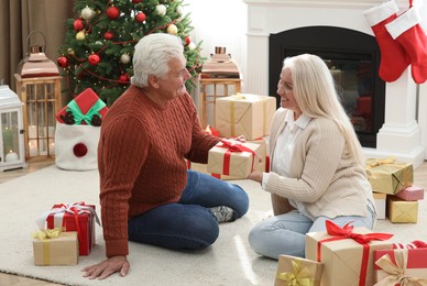 Photo of Happy mature woman presenting Christmas gift to her husband at home