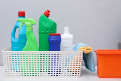 Photo of Basket with detergents and rags on white table against light grey background