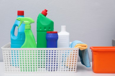 Basket with detergents and rags on white table against light grey background