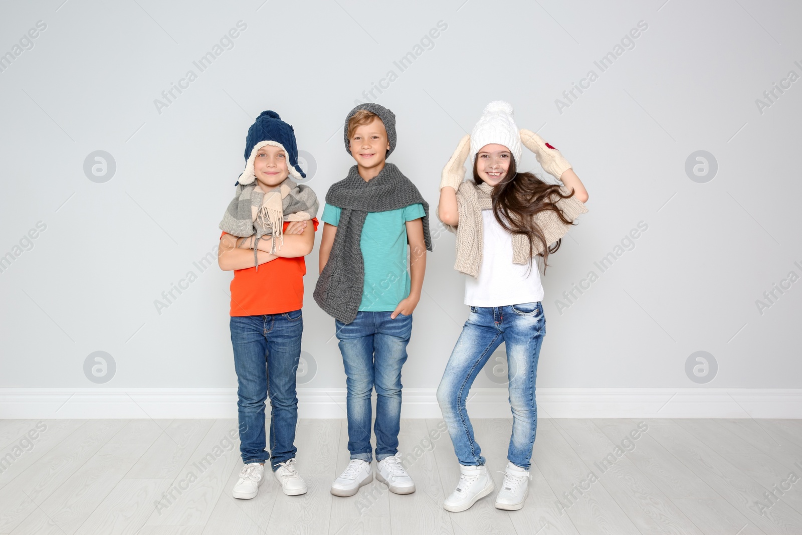 Photo of Cute little children in warm clothes posing near light wall. Christmas celebration