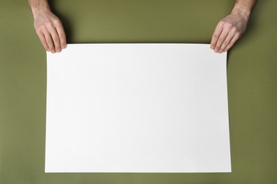Man with empty sheet of paper on olive background, top view. Mockup for design