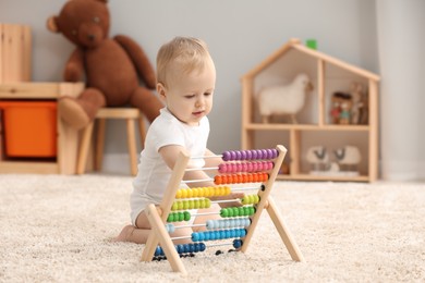 Children toys. Cute little boy playing with wooden abacus on rug at home