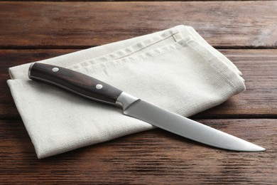 Photo of One sharp knife and napkin on wooden table, closeup