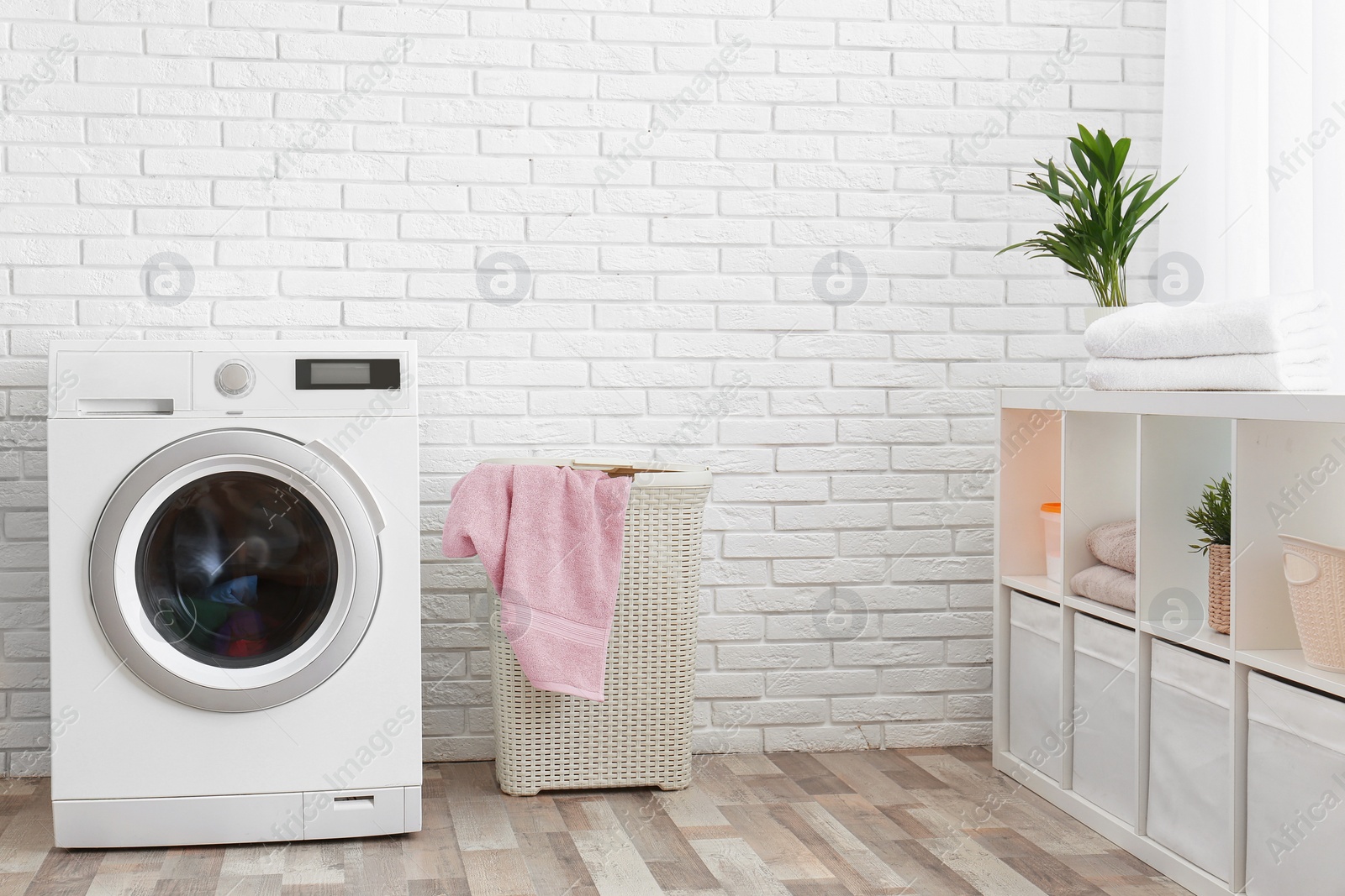 Photo of Modern washing machine near brick wall in laundry room interior, space for text