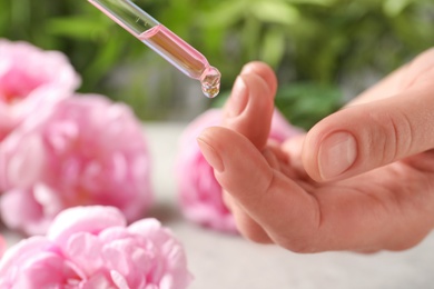 Woman dripping rose essential oil on finger, closeup