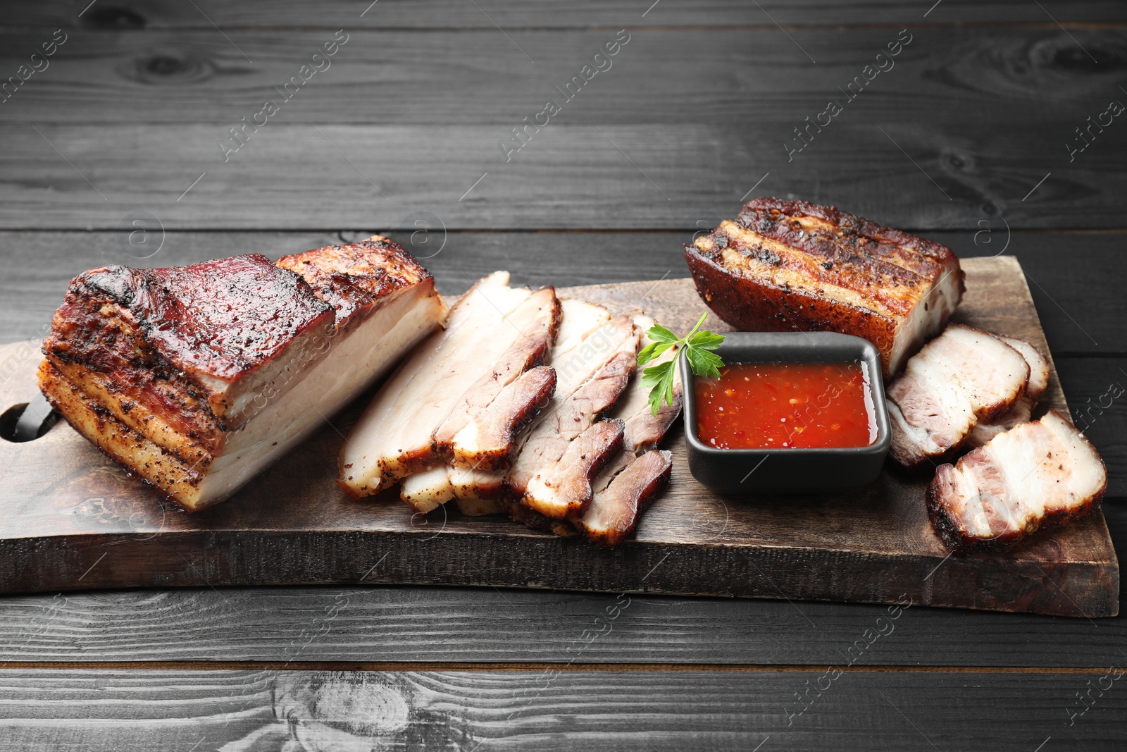 Photo of Pieces of baked pork belly served with sauce and parsley on black wooden table