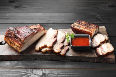 Pieces of baked pork belly served with sauce and parsley on black wooden table