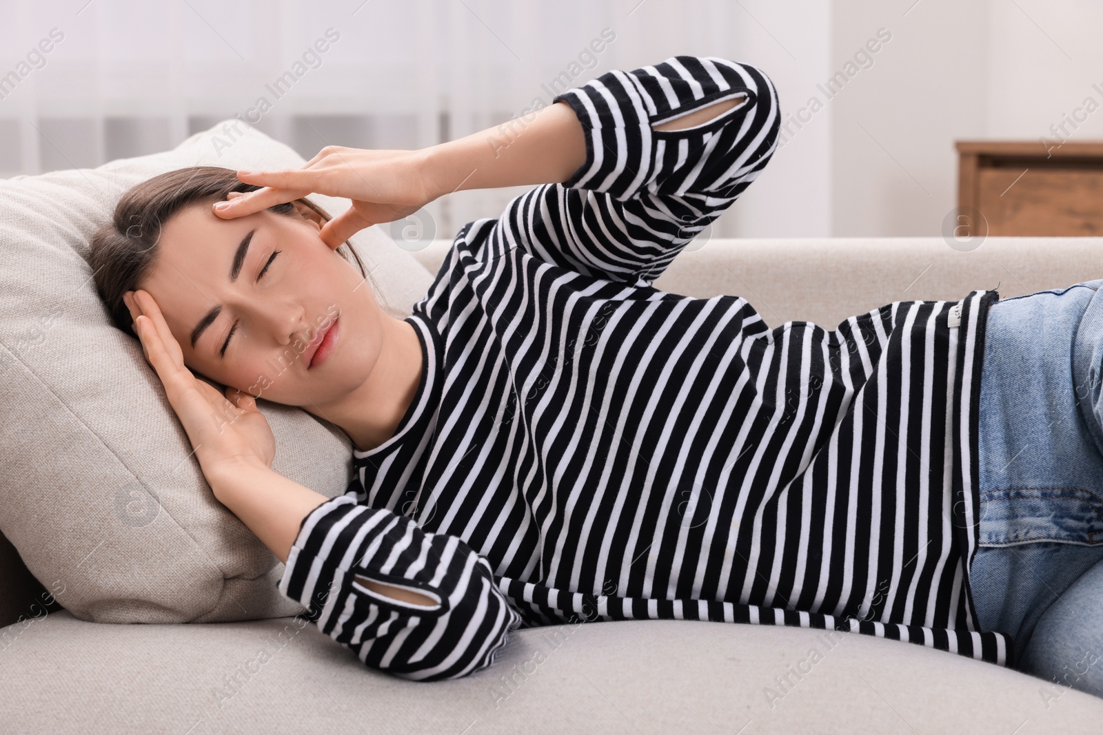 Photo of Sad woman suffering from headache on sofa indoors