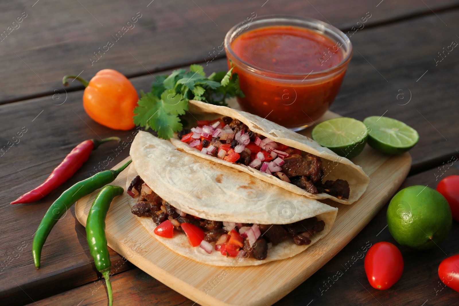 Photo of Delicious tacos with meat, vegetables and sauce on wooden table