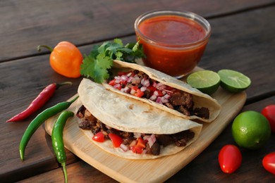 Delicious tacos with meat, vegetables and sauce on wooden table