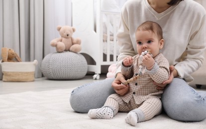 Photo of Young mother and her baby with teether on floor at home. Space for text