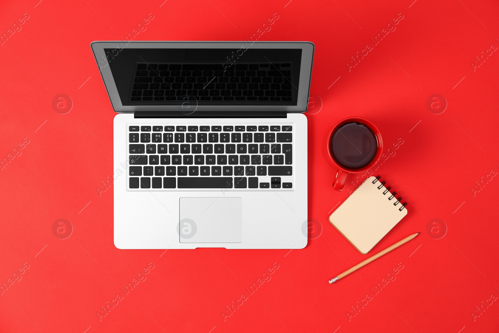 Photo of Modern laptop with cup of coffee and office tools on red background, top view