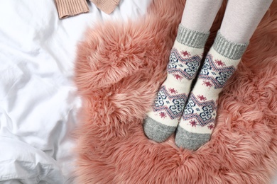 Photo of Woman wearing knitted socks on carpet, top view. Warm clothes