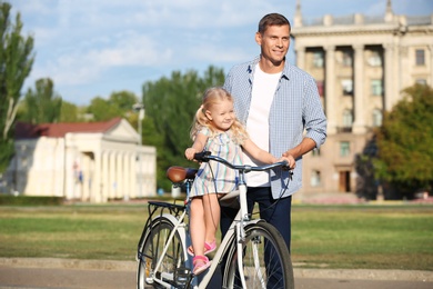 Photo of Happy man and his little daughter with bicycle outdoors on summer day
