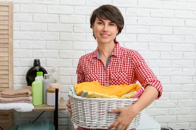 Young woman holding basket with clean clothes at home