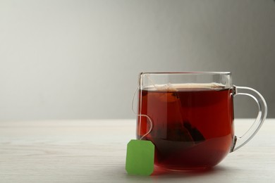 Photo of Tea bag in glass cup of hot water on white wooden table. Space for text