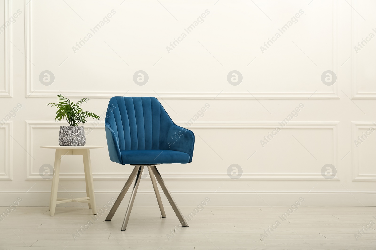 Photo of Modern blue armchair and houseplant on wooden table near white wall indoors. Space for text