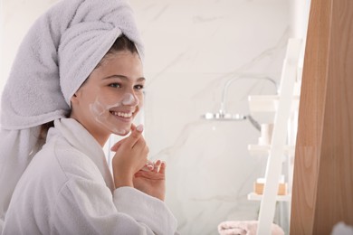 Beautiful teenage girl applying cleansing foam onto face in bathroom. Skin care cosmetic