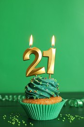 Photo of 21th birthday. Delicious cupcake with number shaped candles for coming of age party on green wooden table
