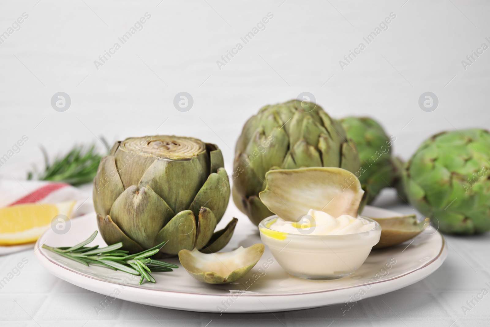 Photo of Delicious cooked artichokes with tasty sauce served on white table, closeup