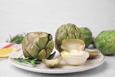 Photo of Delicious cooked artichokes with tasty sauce served on white table, closeup