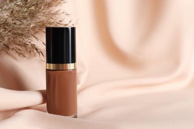 Photo of Bottle of skin foundation and dried reed on beige cloth, closeup with space for text. Makeup product