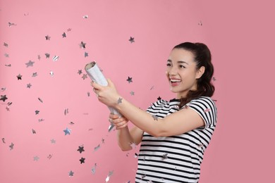 Young woman blowing up party popper on pink background