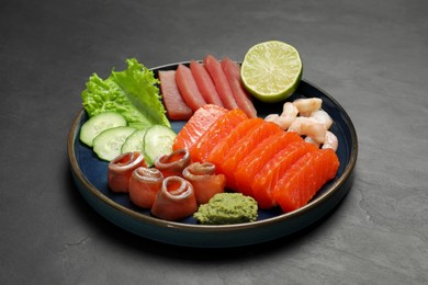 Photo of Tasty salmon slices, shrimp, cucumber and tuna on black table. Delicious sashimi dish