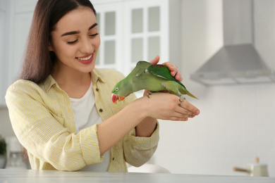 Photo of Young woman with Alexandrine parakeet indoors. Cute pet
