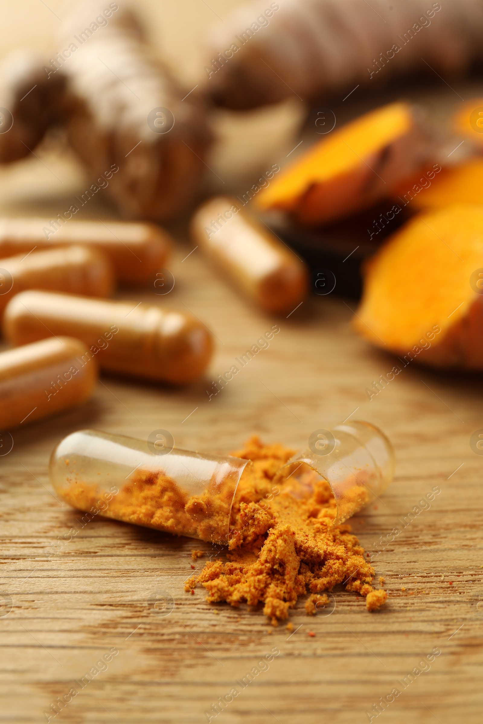 Photo of Aromatic turmeric powder and pills on wooden table, closeup