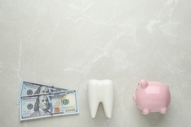 Photo of Ceramic model of tooth, piggy bank and dollar banknotes on light grey table, flat lay with space for text. Expensive treatment