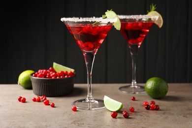 Photo of Tasty cranberry cocktail with rosemary and lime in glasses on grey table against black background