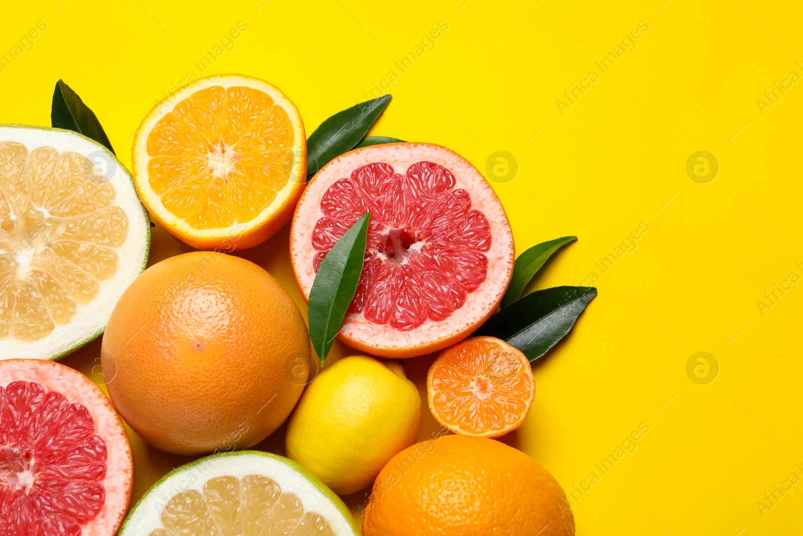 Photo of Different ripe citrus fruits with green leaves on yellow background, flat lay. Space for text