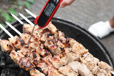 Man measuring temperature of delicious kebab on metal brazier outdoors, closeup