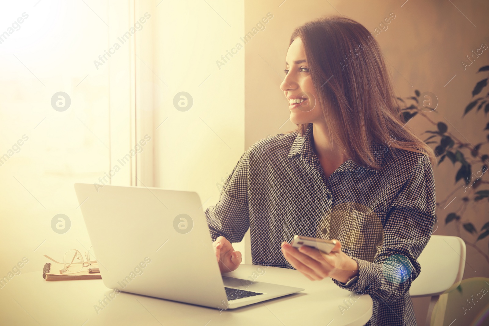 Image of Young woman with smartphone working on laptop at table in cafe