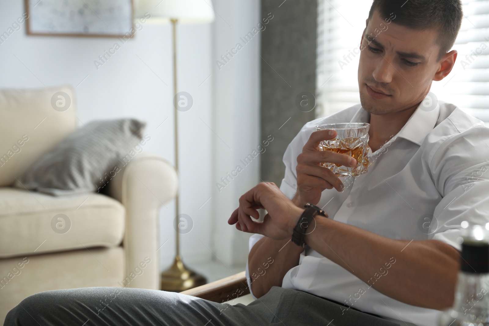 Photo of Young man with glass of whiskey at home. Space for text