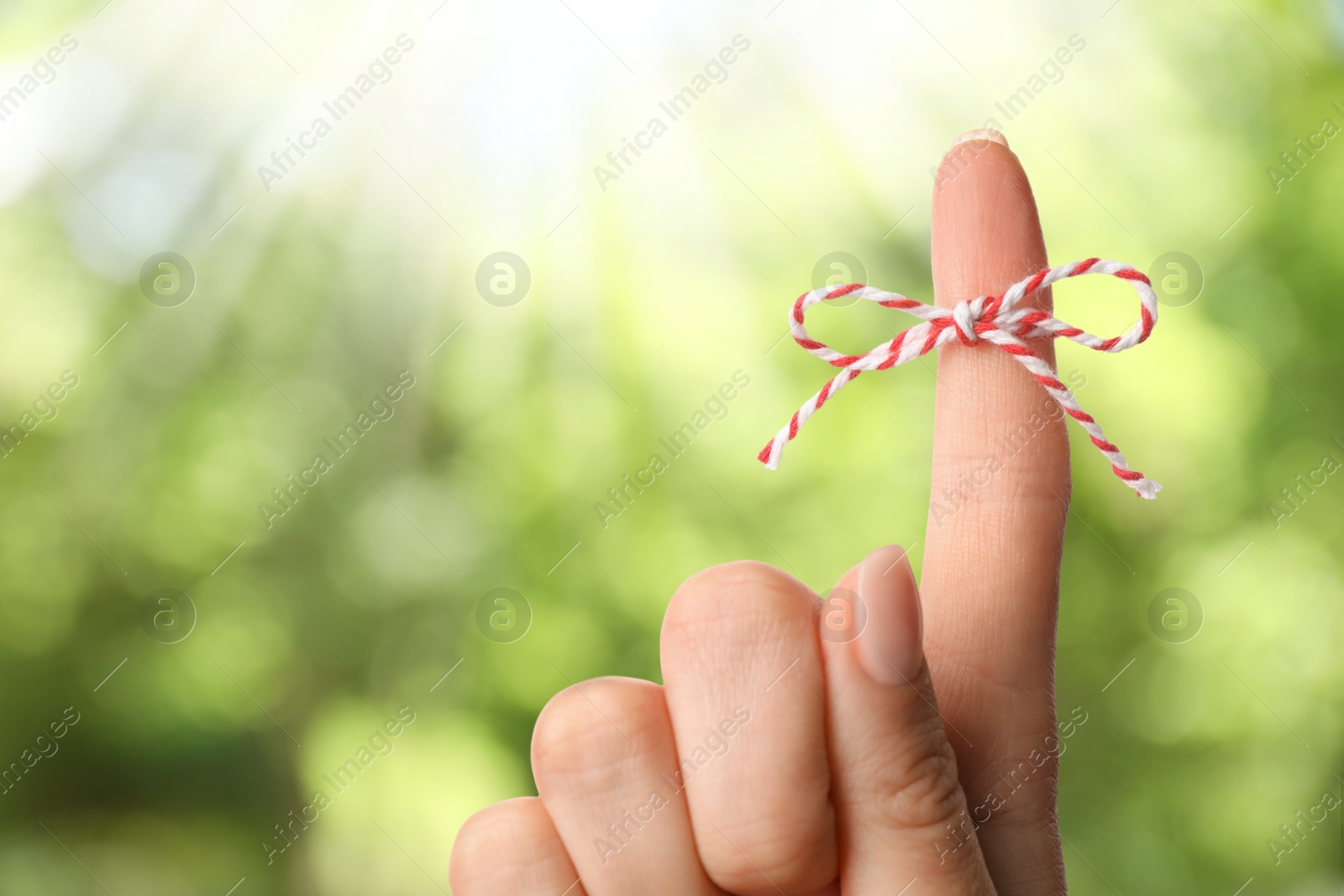 Image of Woman showing index finger with tied bow as reminder on blurred green background, closeup