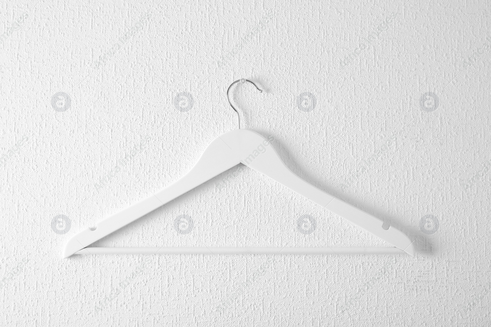 Photo of Empty clothes hanger on light wall. Wardrobe accessory