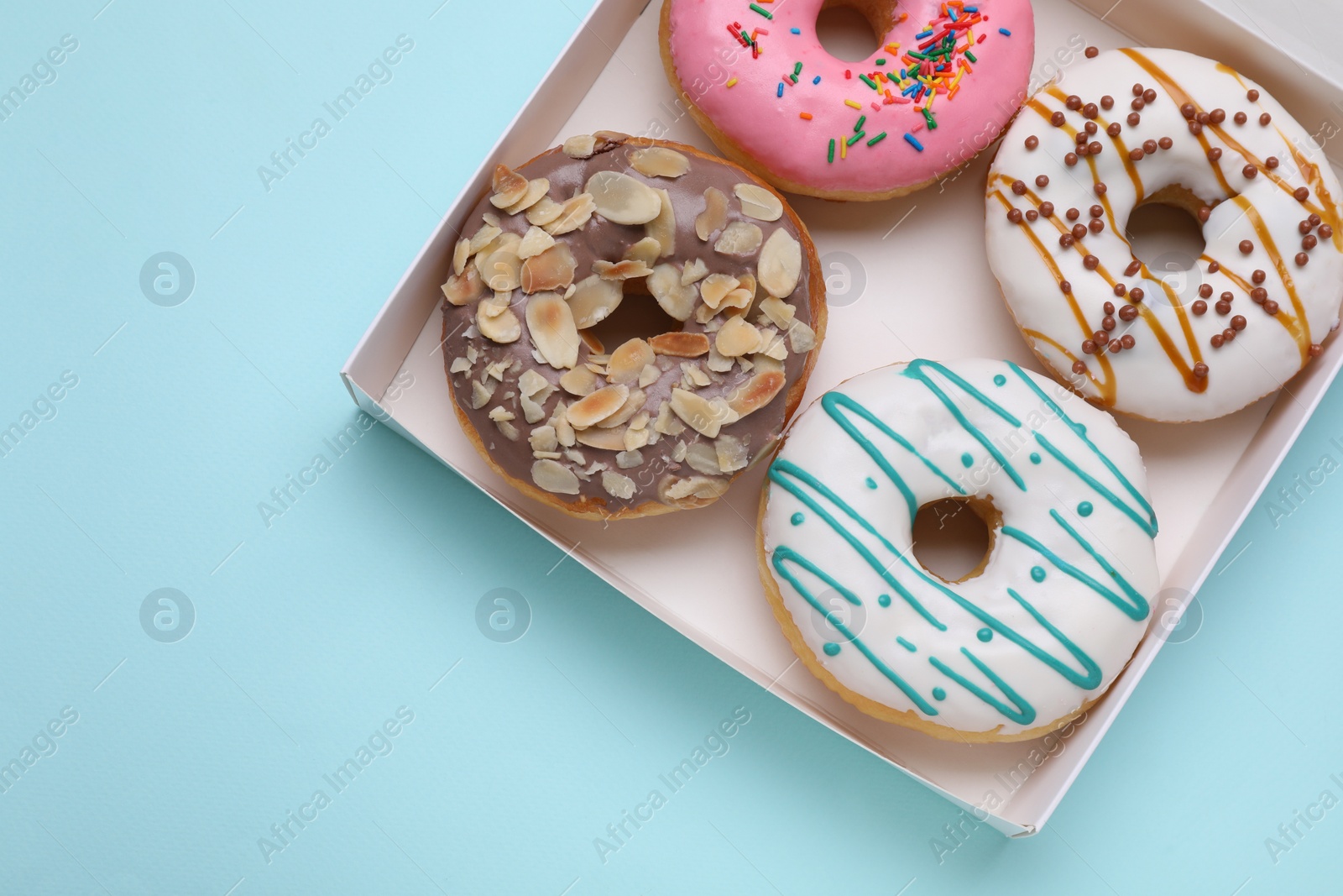 Photo of Box with different tasty glazed donuts on light blue background, top view