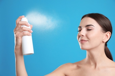 Photo of Young woman applying thermal water on face against color background. Cosmetic product