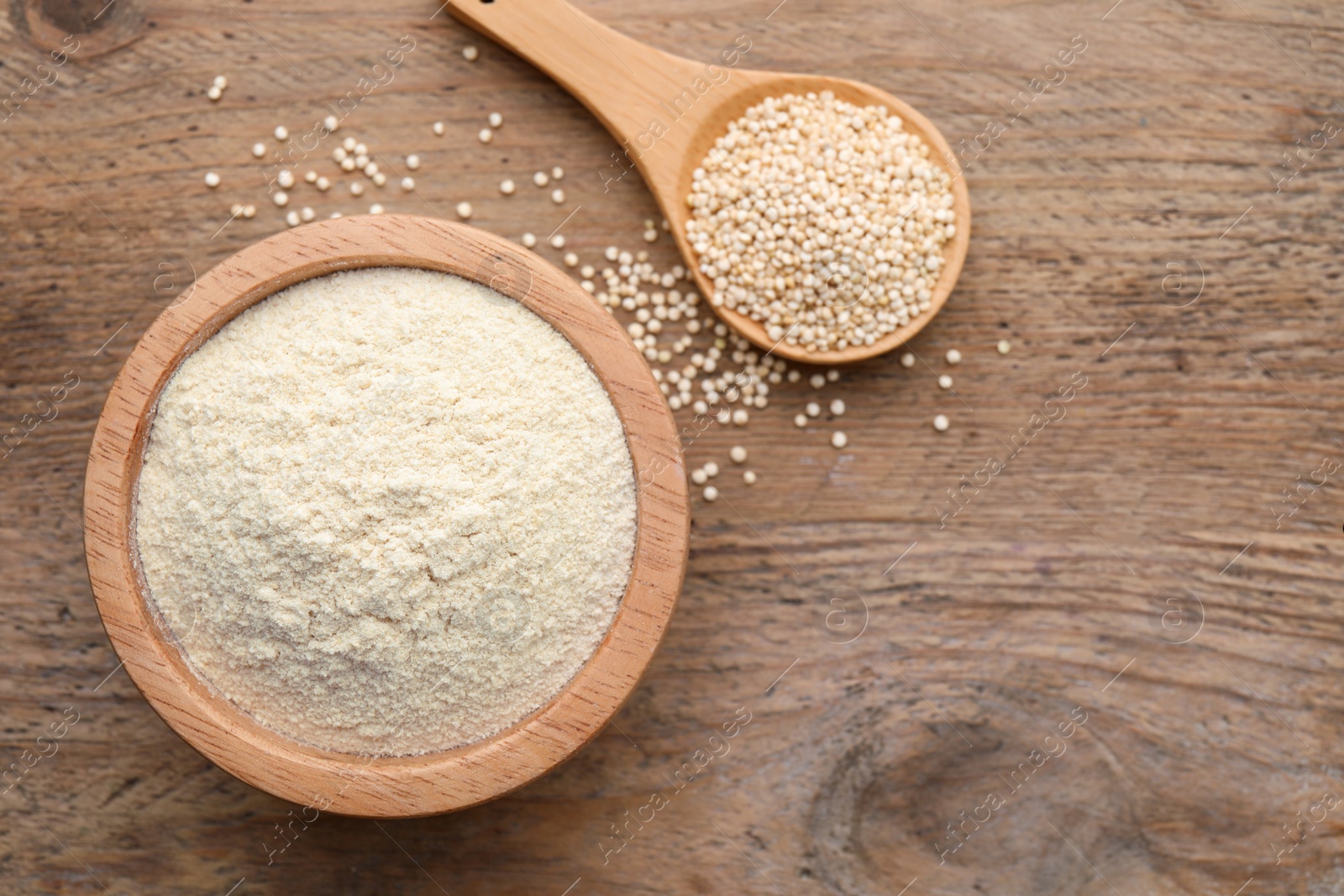 Photo of Quinoa flour in bowl and spoon with seeds on wooden table, flat lay