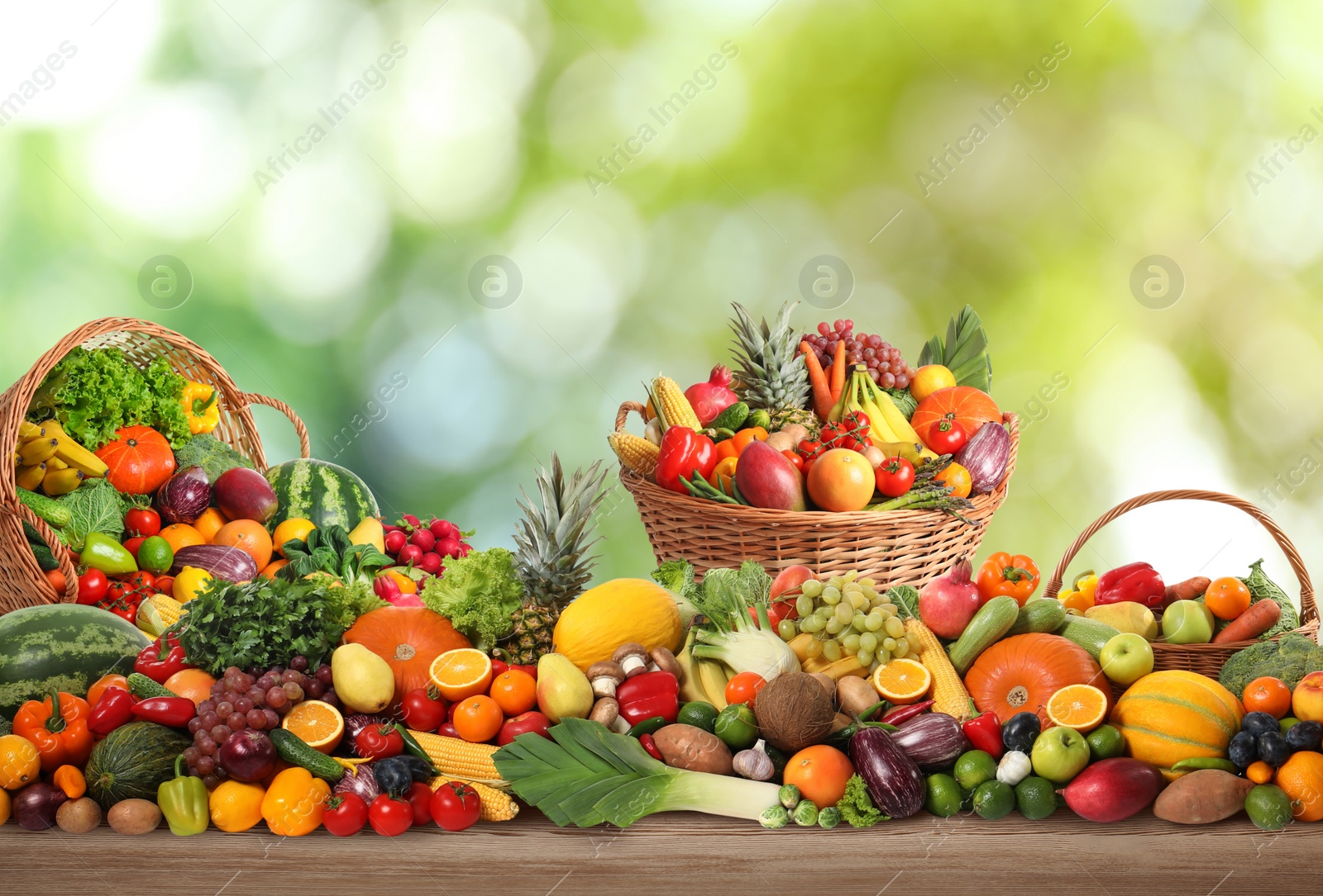 Image of Assortment of fresh organic vegetables and fruits on wooden table against blurred green background