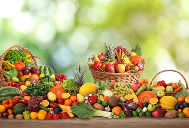 Image of Assortment of fresh organic vegetables and fruits on wooden table against blurred green background