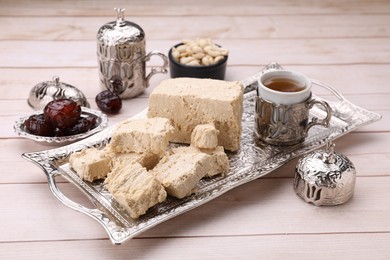 Photo of Pieces of tasty halva, tea and dates on light wooden table