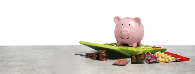 Photo of Piggy bank, calculator, coins and pills on light grey table against white background, space for text. Medical insurance