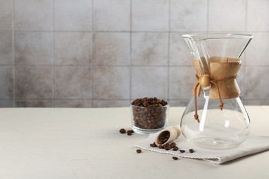 Empty glass chemex coffeemaker and beans on white table, space for text