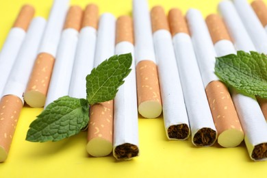 Photo of Menthol cigarettes and mint on yellow background, closeup