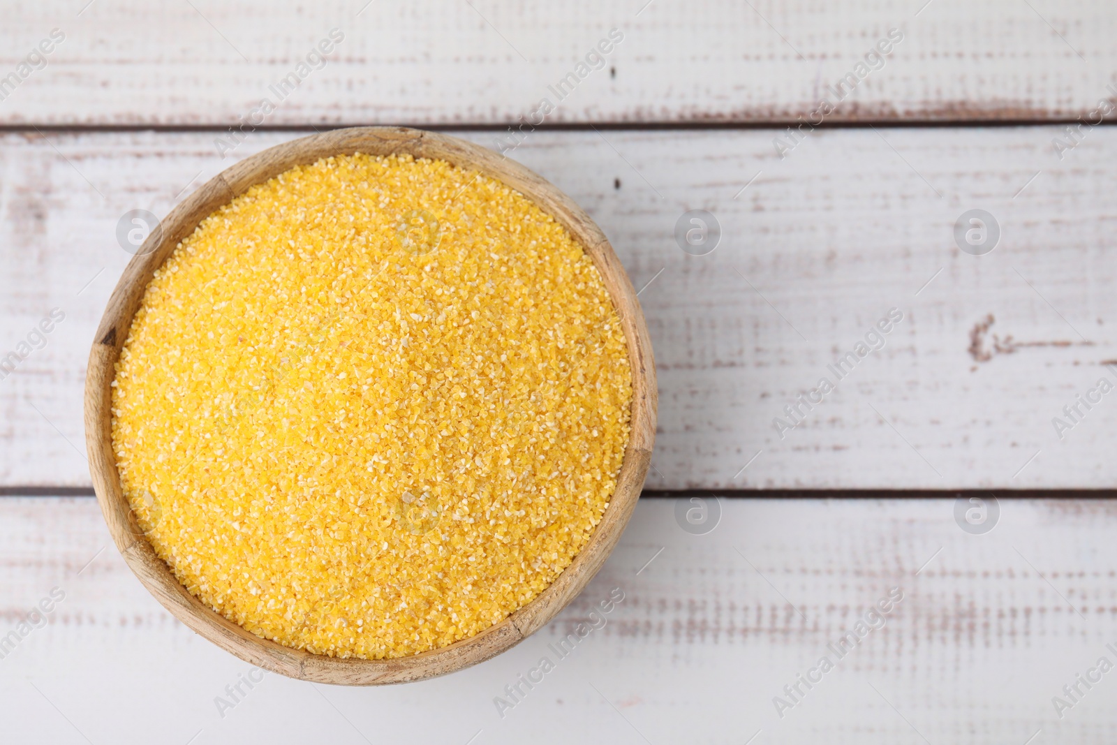 Photo of Raw cornmeal in bowl on light wooden table, top view. Space for text