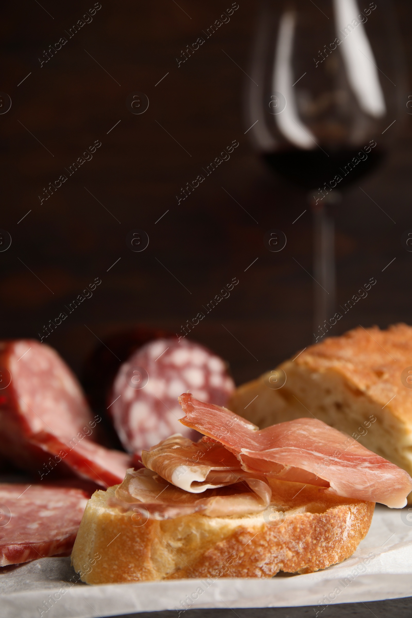 Photo of Delicious bread with prosciutto and other sausages on paper, closeup. Space for text